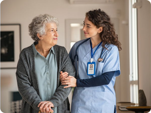 Female medical worker with her arm interlocked with an elderly woman helping her walk